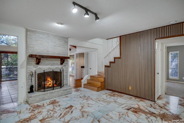 unfurnished living room with a fireplace, track lighting, and a textured ceiling