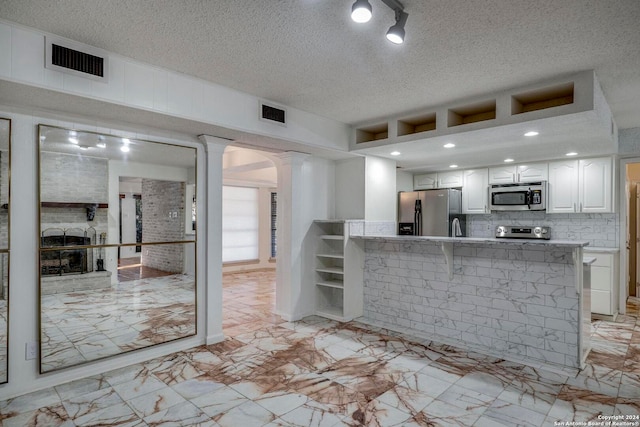 kitchen with white cabinets, a textured ceiling, stainless steel appliances, and kitchen peninsula