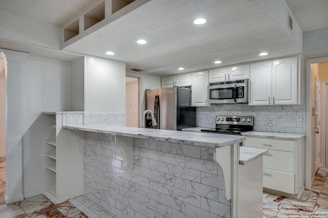 kitchen with white cabinets, a breakfast bar, kitchen peninsula, and appliances with stainless steel finishes