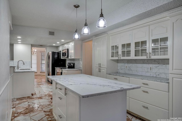 kitchen featuring sink, a textured ceiling, appliances with stainless steel finishes, a kitchen island, and white cabinetry