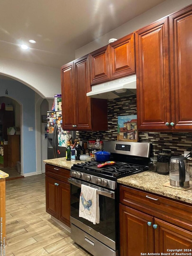 kitchen featuring backsplash, light stone countertops, stainless steel appliances, and light hardwood / wood-style floors