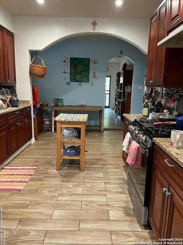 kitchen featuring range hood, light stone counters, light hardwood / wood-style flooring, and stainless steel gas range