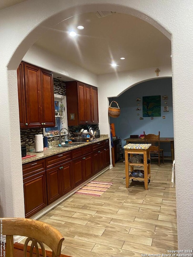 kitchen featuring decorative backsplash, light stone counters, light hardwood / wood-style flooring, and sink