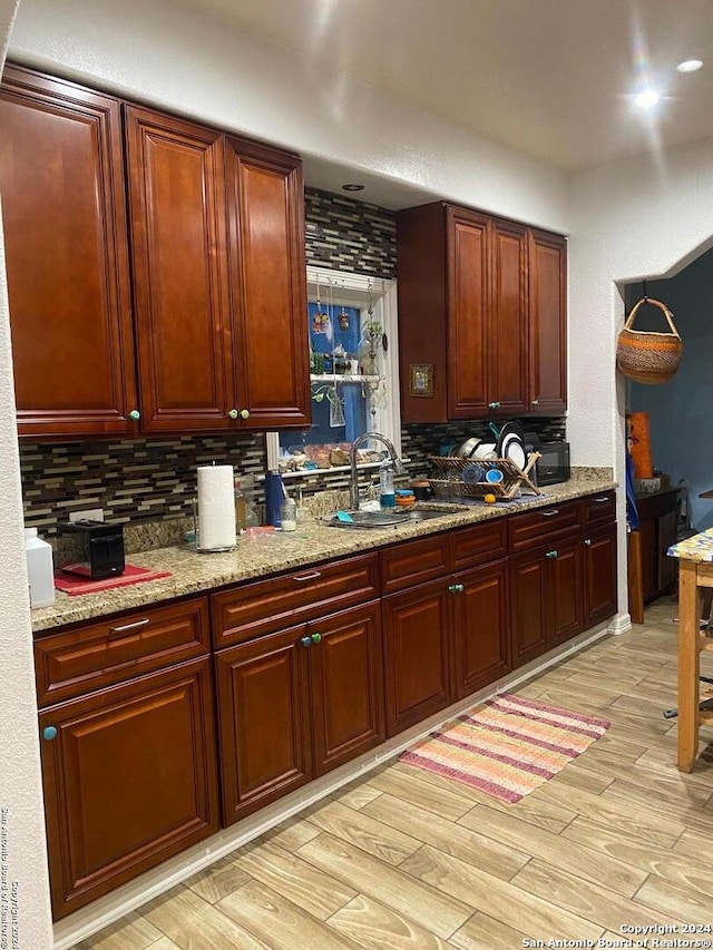 kitchen featuring tasteful backsplash, light stone counters, sink, and light wood-type flooring