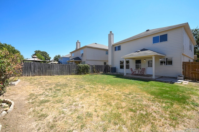 rear view of property featuring a lawn, central AC unit, and a patio area