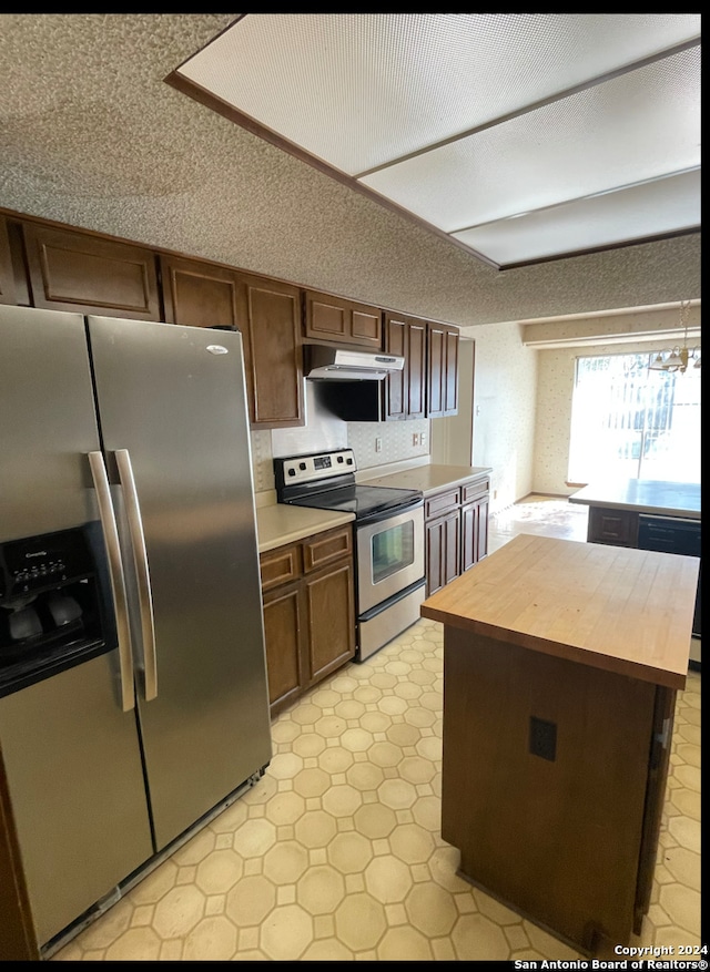 kitchen with dark brown cabinetry, butcher block countertops, a textured ceiling, a kitchen island, and appliances with stainless steel finishes