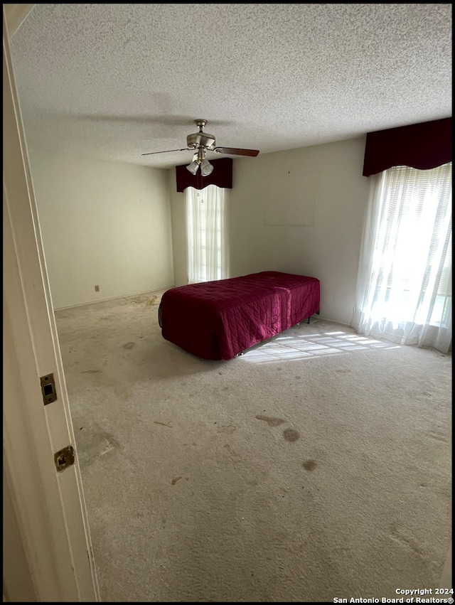 unfurnished bedroom featuring carpet, a textured ceiling, and ceiling fan