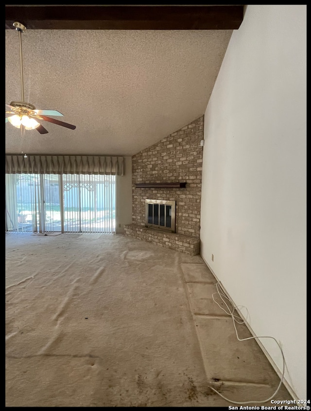 unfurnished living room with a textured ceiling, lofted ceiling with beams, a brick fireplace, and ceiling fan