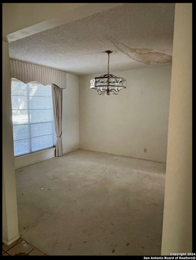 unfurnished dining area featuring a textured ceiling and an inviting chandelier