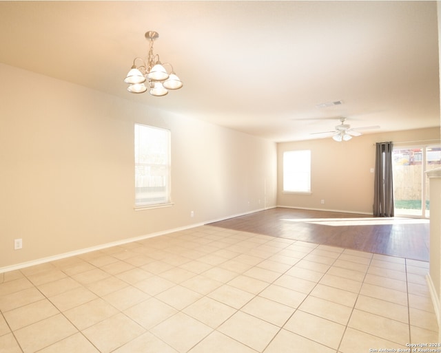 spare room with ceiling fan with notable chandelier, a wealth of natural light, and light hardwood / wood-style flooring