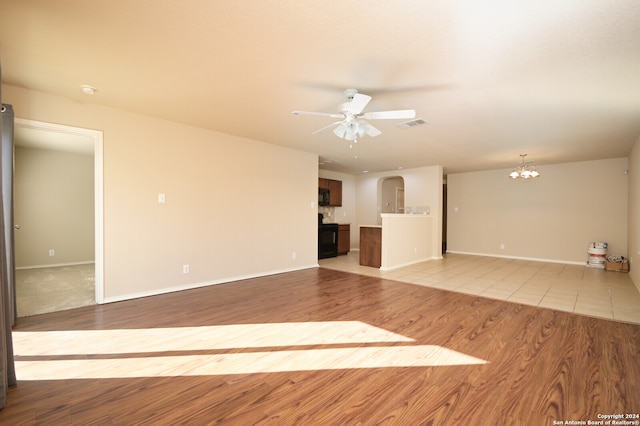 unfurnished living room with ceiling fan with notable chandelier and light hardwood / wood-style floors