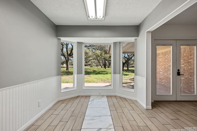 entryway with a textured ceiling, light hardwood / wood-style flooring, and french doors