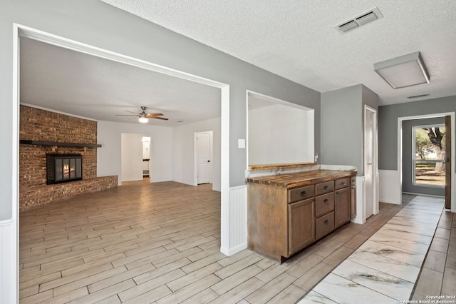 kitchen featuring a fireplace, a textured ceiling, light hardwood / wood-style flooring, and ceiling fan