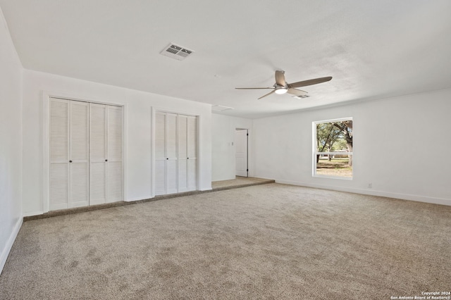 unfurnished bedroom featuring carpet, ceiling fan, and two closets