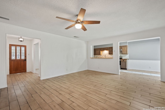 unfurnished living room with ceiling fan, a textured ceiling, and light hardwood / wood-style flooring