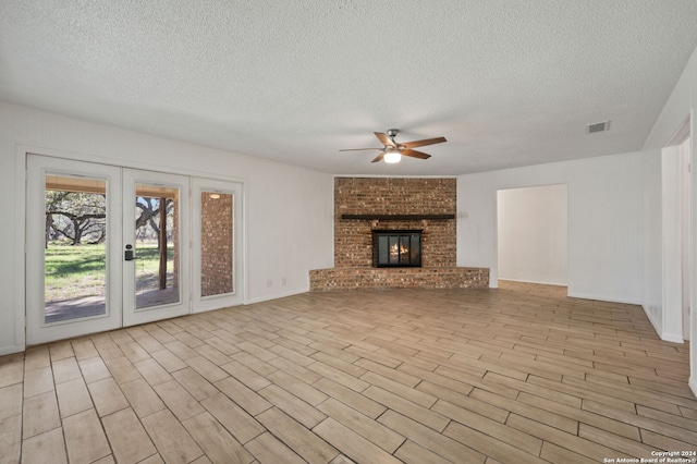 unfurnished living room featuring ceiling fan, a fireplace, light hardwood / wood-style floors, and a textured ceiling