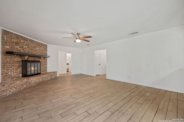 unfurnished living room featuring ceiling fan, a fireplace, a textured ceiling, and light hardwood / wood-style flooring