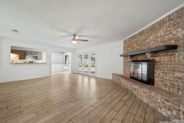 unfurnished living room with ceiling fan, a fireplace, a textured ceiling, and light wood-type flooring