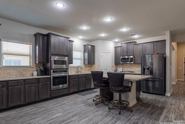 kitchen with a textured ceiling, a center island, dark brown cabinetry, and stainless steel appliances