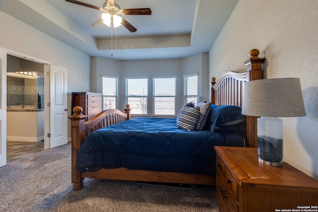 bedroom with carpet flooring, ceiling fan, a tray ceiling, and ensuite bath