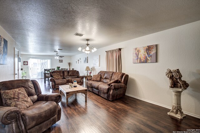 living room with ceiling fan with notable chandelier, dark hardwood / wood-style flooring, and a textured ceiling