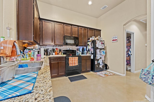 kitchen featuring black appliances, light stone counters, dark brown cabinetry, and sink