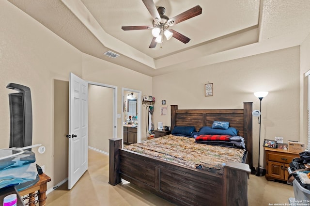 carpeted bedroom featuring ceiling fan, a textured ceiling, connected bathroom, and a tray ceiling