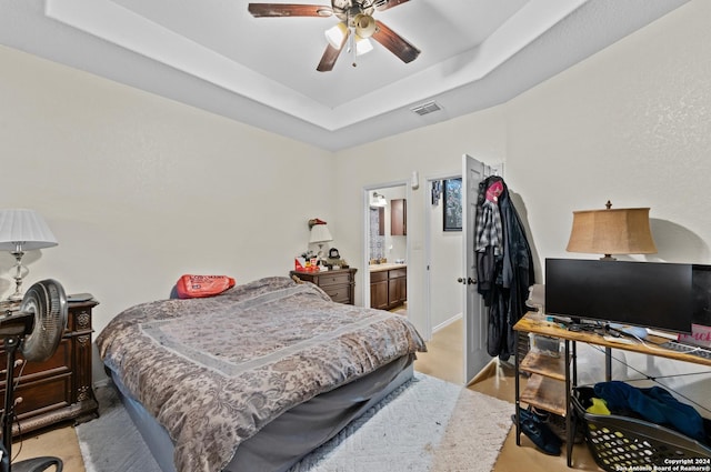 bedroom featuring ceiling fan, ensuite bathroom, and a tray ceiling