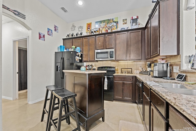 kitchen featuring light stone countertops, dark brown cabinetry, decorative backsplash, and black appliances