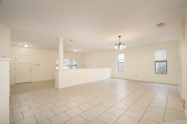 unfurnished room featuring a notable chandelier, light tile patterned floors, and ornate columns