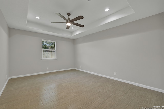 empty room featuring ceiling fan, light wood-type flooring, and a tray ceiling