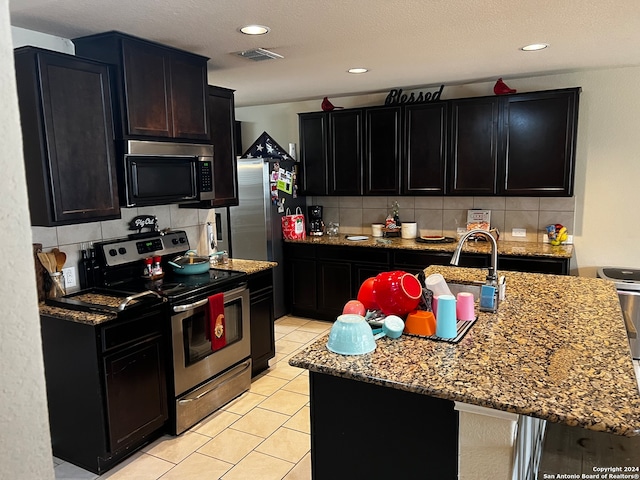 kitchen with decorative backsplash, a kitchen island with sink, sink, and appliances with stainless steel finishes