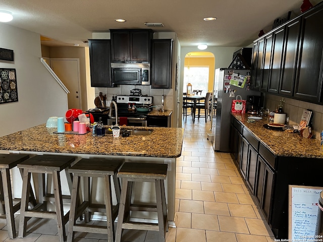 kitchen featuring stone counters, appliances with stainless steel finishes, backsplash, and a kitchen island with sink