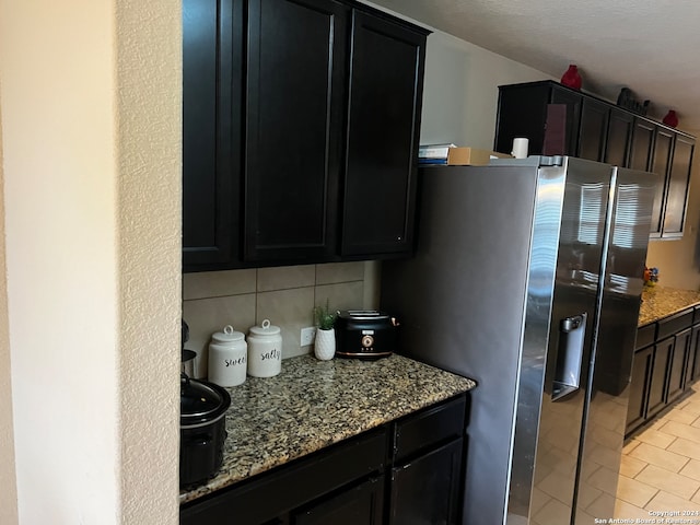 kitchen featuring decorative backsplash, light tile patterned flooring, light stone counters, and stainless steel refrigerator with ice dispenser