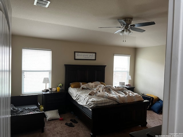 carpeted bedroom with a textured ceiling, multiple windows, and ceiling fan