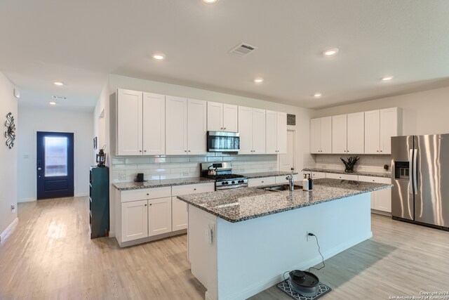 kitchen with appliances with stainless steel finishes, white cabinetry, and an island with sink