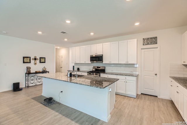 kitchen with appliances with stainless steel finishes, white cabinetry, dark stone countertops, and an island with sink