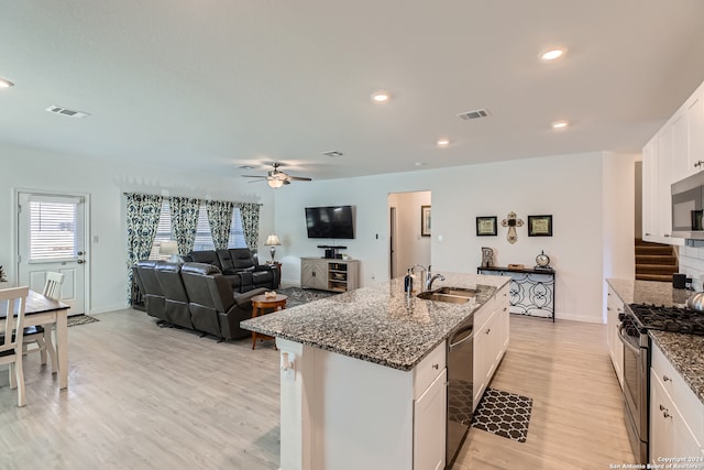 kitchen with dark stone countertops, light hardwood / wood-style floors, a kitchen island with sink, white cabinets, and appliances with stainless steel finishes