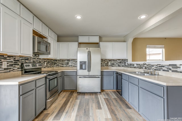 kitchen with sink, decorative backsplash, gray cabinets, wood-type flooring, and stainless steel appliances