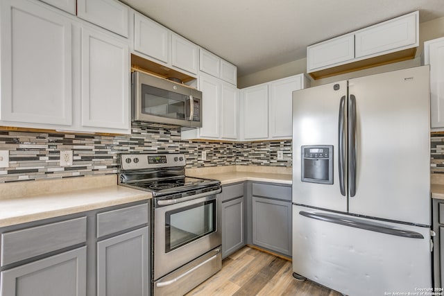 kitchen featuring gray cabinetry, light hardwood / wood-style flooring, decorative backsplash, appliances with stainless steel finishes, and white cabinetry