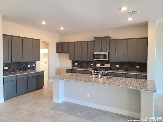 kitchen with light stone counters, arched walkways, stainless steel appliances, tasteful backsplash, and a sink