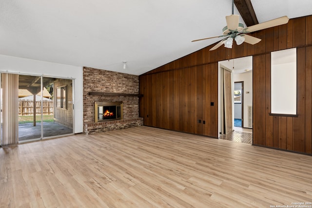 unfurnished living room featuring lofted ceiling with beams, light hardwood / wood-style floors, wooden walls, and a brick fireplace