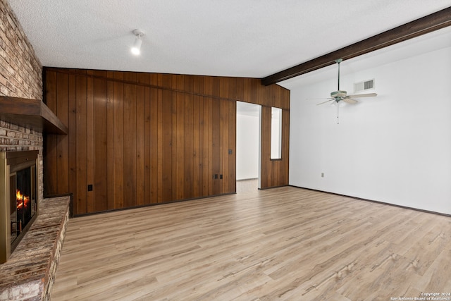 unfurnished living room with vaulted ceiling with beams, light hardwood / wood-style flooring, a textured ceiling, wooden walls, and a fireplace