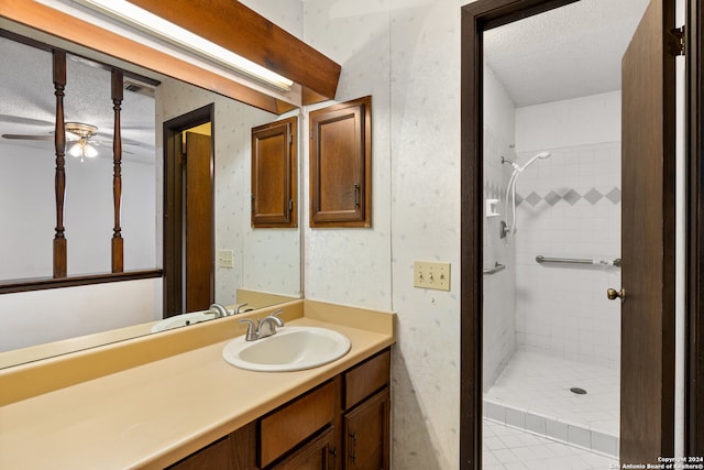 bathroom with a textured ceiling, ceiling fan, tiled shower, and vanity