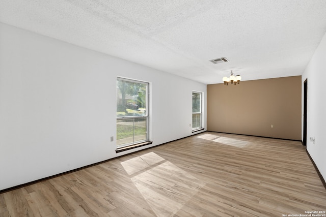 spare room with a textured ceiling, a notable chandelier, and light wood-type flooring