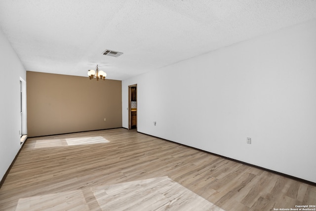 unfurnished room featuring light hardwood / wood-style floors, a textured ceiling, and a notable chandelier