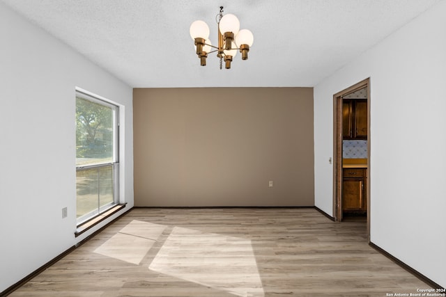 unfurnished room featuring a textured ceiling, light wood-type flooring, plenty of natural light, and a notable chandelier