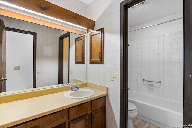 full bathroom featuring vanity, tiled shower / bath, hardwood / wood-style flooring, toilet, and a textured ceiling