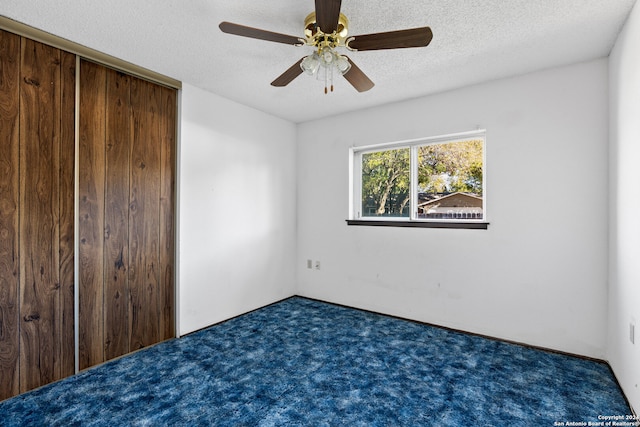 unfurnished bedroom featuring a textured ceiling, a closet, dark carpet, and ceiling fan