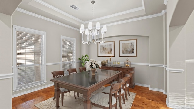 dining area featuring an inviting chandelier, a tray ceiling, light hardwood / wood-style flooring, and crown molding